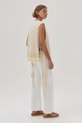 Chaleco tejido de algodón color beige, con escote en V, lazos laterales y terminaciones con pompones.