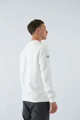 Buzo blanco de felpa con cuello redondo, mangas largas y puños. Presenta un estampado en relieve con texto y logo en goma.