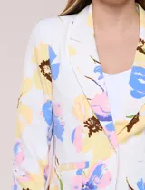 Blazer de silueta semientallada confeccionado en tela sastrera de color blanco con estampado floral en tonos amarillos, celestes, rosados y azules. Presenta solapa de muesca clásica, acceso frontal mediante un botón a tono, bolsillos simulados con solapa y mangas largas de corte clásico.