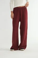 Pantalón de tejido de punto en color bordó, de corte amplio y tiro alto. Presenta cintura elástica con cordón de ajuste y costuras verticales decorativas a lo largo de las piernas.
