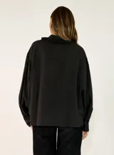 Camisa negra de corte holgado con cuello tipo bebé con volados y lazo de ajuste, cierre frontal con botones y mangas largas abullonadas con puños abotonados.