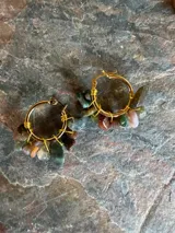 Aros de tipo argolla dorados decorados con pequeñas piedras naturales colgantes en tonos multicolores.