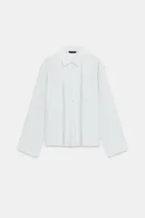 Camisa de cuello solapa y manga larga con puños anchos. Presenta un diseño con pliegues verticales en el frente y cierre frontal con botones tipo perla.