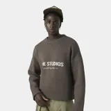 Sweater de punto grueso color marrón oscuro, con corte cuadrado y ligeramente corto. Presenta cuello redondo, puños y ruedo acanalados, y el logo de la marca Eme Studios junto a la frase 'curated by ben ice' en jacquard color crema en el frente.