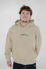 Canguro color beige con capucha, bolsillo tipo canguro y estampado con la frase "Wear More & Worry Less" en el pecho.