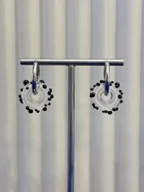 Aros tipo argolla con dije de vidrio en forma de dona transparente con pequeñas esferas negras decorativas, montados sobre base de plata 925.