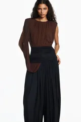 Mono largo bicolor con cuerpo drapeado en color marrón y parte inferior tipo pantalón bombacho en color negro. Presenta un diseño sin mangas con un hombro descubierto y una banda ancha ajustada en la cintura.