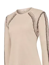 Remera de manga larga color beige, confeccionada en tejido de punto tipo waffle. Presenta detalles artesanales de crochet en tono marrón oscuro a lo largo de las mangas, hombros y puños, con cuello redondo.