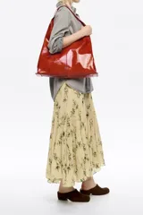 Bolso de hombro de tamaño maxi confeccionado en piel vacuna con acabado brillante. Presenta una estructura blanda, asa de hombro integrada y logo metálico de la marca en la parte inferior. Incluye bolsillo interior y cierre de cordón.