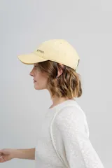 Gorra verde militar de diseño clásico con visera curva y aplique metálico plateado con la inscripción "Peach" en el lateral frontal. Cuenta con tira ajustable en la parte trasera.