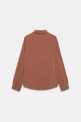 Camisa celeste de manga larga con cuello solapa y pliegues en los puños. Presenta cierre frontal con botones forrados al tono y bajo asimétrico.