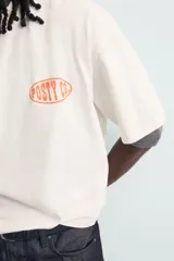 Camiseta de corte relajado color crudo, con cuello redondo y manga corta. Presenta un estampado gráfico pequeño en el pecho y un diseño grande en la espalda relacionado con el artista Post Malone.