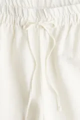 Pantalón de corte holgado en tejido liviano de mezcla de lino. Modelo de tiro alto con cintura elástica y cordón para ajustar fino, bolsillos laterales discretos y piernas rectas.