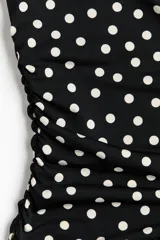 Vestido midi entallado de punto elástico en color negro con estampado de lunares blancos. Presenta escote bote, mangas japonesas y laterales fruncidos que realzan la silueta.