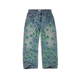 Pantalón de jean estilo baggy, color azul claro, con múltiples parches bordados en forma de estrella con la inscripción 'All Star' en color verde. Posee cordones colgantes en la cintura y cierre frontal.