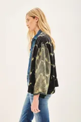 Kimono de estilo abierto con mangas amplias, confeccionado en viscosa con técnica de teñido tie-dye en tonos negro y verde oliva. Presenta una guarda frontal bordada con detalles de pedrería y apliques decorativos.