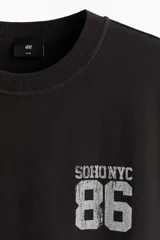 Remera de algodón en punto pesado color negro, de corte holgado con hombros caídos, cuello redondo acanalado y estampa frontal estilo universitario con el texto 'SOHO NYC 86'.