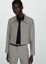 Chaqueta corta de diseño recto y estilo sastrero, confeccionada en tejido fluido color gris. Presenta cuello camisero, cierre frontal con botones ocultos y dos bolsillos de parche en el frente.