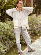 Cardigan de punto color beige con escote en V, cierre frontal con botones, bolsillos delanteros aplicados y detalle de flecos en el ruedo.