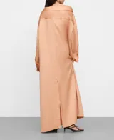 Vestido camisero midi de tejido satinado en tono salmón, con cuello italiano desestructurado, mangas largas con puños abotonados y una original botonadura frontal asimétrica.