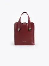 Cartera tipo tote de tamaño pequeño, confeccionada en cuero color bordó. Presenta doble asa de mano y detalles metálicos plateados en forma de llama en la unión de las asas con el cuerpo de la cartera. Incluye el logo de la marca estampado en la parte inferior frontal.