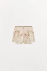 Shorts de tiro bajo con cintura elástica, confeccionados en tejido georgette de viscosa. Presentan un diseño delicado con bordados florales y aplicaciones de encaje a contraste en el ruedo.