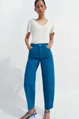 Jeans de tiro alto con corte tapered y largo al tobillo. Presenta cinco bolsillos, trabillas en la cintura, cierre frontal con cremallera y botón, y detalle de raya planchada en el frente.
