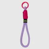 Llavero tipo correa de mano confeccionado en cordón de nylon color lila, con detalle de nudo en color fucsia y mosquetón circular metálico. Incluye una etiqueta textil negra con el logo de la marca en color verde lima.