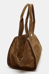 Bolso de mano de formato alargado, confeccionado en serraje (gamuza) color marrón. Presenta doble asa de hombro y cierre principal mediante cremallera. Incluye un bolsillo interior con cremallera.