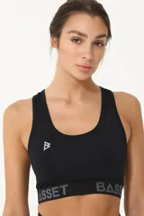 Top deportivo negro con logo blanco en el frente y banda elástica con letras grises en el bajo busto.