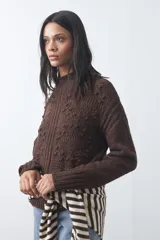 Polera de tejido de punto color marrón, con cuello alto y diseño de textura con relieves y trenzas. Posee mangas largas con puños acanalados.
