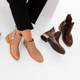 Botas cortas de cuero vacuno color marrón, con diseño de caña baja y cierre metálico en ambos laterales. Presentan un taco cuadrado de madera y suela de goma.