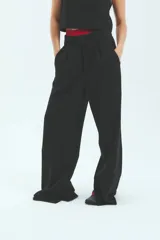 Pantalón sastrero negro de crepe con corte oversize, bolsillos laterales y tajo en la botamanga interna.