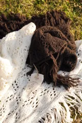 Bufandón triangular tejido en lana merino, con diseño calado y terminaciones con flecos largos en los extremos. Versátil para usar como bufanda o chal.