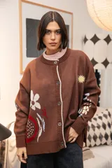 Saco tejido de punto color marrón con diseño de motivos orgánicos y florales. Presenta cierre frontal con botones, cuello redondo y mangas largas con puños acanalados. El diseño incluye detalles bordados que aportan textura y profundidad a la prenda.