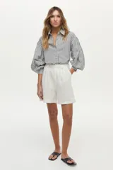 Camisa de algodón con rayas verticales grises y blancas, cuello camisero, mangas largas abullonadas y cierre frontal con botones.