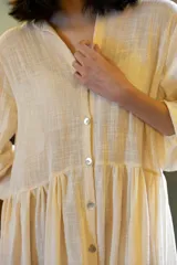 Vestido largo de muselina color crema, con silueta amplia y fluida. Presenta cuello en V, cierre frontal con botones y mangas largas relajadas.