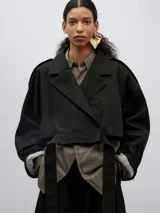 Chaqueta corta negra con cuello solapa, mangas capa en espalda, largo irregular y cinturón.