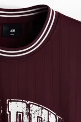 Remera bordó de punto acanalado con corte holgado, cuello redondo con ribete rayado y estampa frontal estilo universitario con la inscripción "GOLDEN" y el número "22" en blanco.