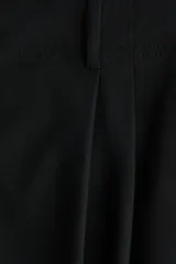 Pantalón negro de tiro medio con corte holgado y diseño de piernas globo, pinzas en la parte delantera y puños elásticos ajustados en los tobillos. Cuenta con cierre frontal y trabillas para cinturón.