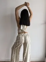 Top de cuello halter con escote en V profundo y bajo en punta. Presenta un diseño de rayas horizontales irregulares en color marrón sobre fondo beige y se ajusta mediante lazos en el cuello y la espalda.