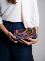 Billetera de tela bordada con diseño de ave multicolor. Tiene cierre de cremallera y tirador con pompón amarillo.