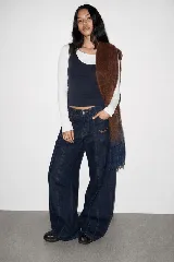 Pantalón de jean azul oscuro de corte baggy, con tiro medio, bolsillos frontales aplicados con detalles bordados y costuras verticales destacadas a lo largo de las piernas.