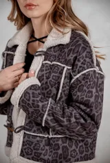 Campera de gamuza con estampado animal print en tonos grises, forrada con corderito sintético en color crema. Presenta cierre frontal con botones tipo toggle y detalles de costuras visibles.
