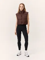 Chaleco puffer de corte cropped y diseño acolchado, con cuello alto y cierre frontal completo. Presenta un acabado liso en color marrón oscuro.