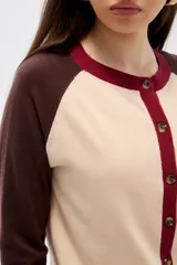 Cardigan de punto con diseño color block, presenta cuerpo en color celeste, mangas en color bordó y detalles de botones y bordes en color rosado. Posee cuello redondo y mangas largas.