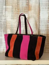 Bolso tipo shopper de cuero y gamuza, con diseño de franjas verticales en marrón, fucsia y naranja. Cuenta con doble asa superior de hombro y cierre superior.