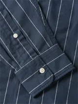 Camisa azul marino con diseño de rayas verticales blancas, de manga larga, corte amplio, cuello clásico y bolsillo de parche en el pecho con el logo bordado.