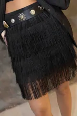 Pollera corta negra de rafia cubierta de flecos en capas. Se complementa con un cinturón negro con apliques metálicos.
