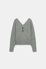 Jersey de punto color gris, con cuello en pico pronunciado y manga larga. Presenta cierre frontal parcial con dos botones y terminaciones en rib.